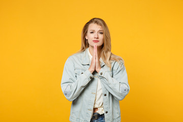 Portrait of pleading young woman in denim casual clothes looking camera, holding hands folded,...