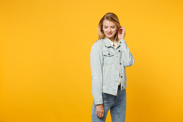 Fototapeta premium Portrait of tender attractive pretty young woman in denim casual clothes touching hair, keeping eyes closed isolated on bright yellow orange background. People lifestyle concept. Mock up copy space.