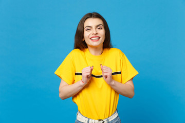 Portrait of smiling happy pretty young woman in vivid casual clothes looking camera and clenching fists isolated on bright blue wall background in studio. People lifestyle concept. Mock up copy space.