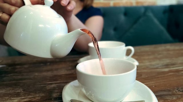 Woman pours tea in a white cup.