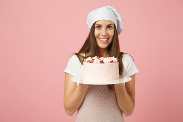 Housewife female chef cook confectioner or baker in apron white t-shirt, toque chefs hat hold in hand cake on stand plate isolated on pink pastel background in studio. Mock up copy space food concept