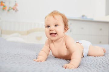 A smiling baby is lying on a bed in a room.