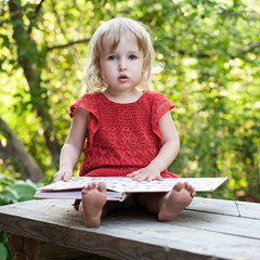 little girl thoughtfully sitting on a bench with big book closeup view