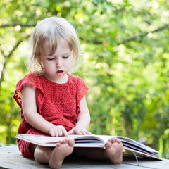 Fototapeta na wymiar little girl thoughtfully sitting on a bench with big book closeup view