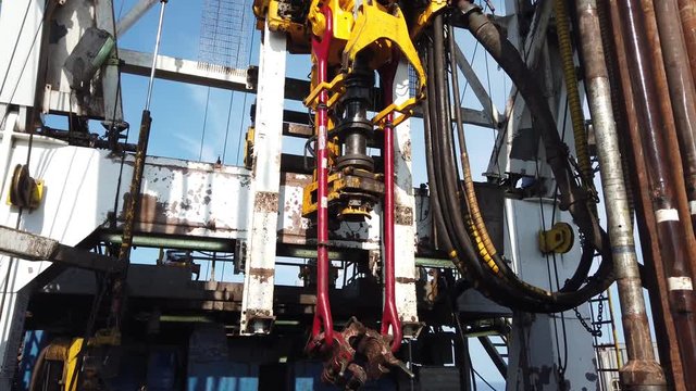 Top Drive System (TDS) moving along the dolly track of derrick while drilling an oil well for oil and gas exploration and production. View from back of oil derrick.