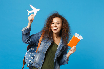 Young african american girl teen student in denim clothes, backpack hold pass isolated on blue wall background studio portrait. Education in high school university college concept. Mock up copy space.