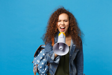 Young african american girl teen student in denim clothes, backpack hold megaphone isolated on blue...