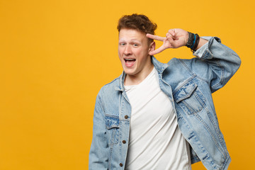 Obraz premium Portrait of cheerful young man in denim casual clothes keeping mouth open showing victory sign isolated on yellow orange wall background. People sincere emotions lifestyle concept. Mock up copy space.