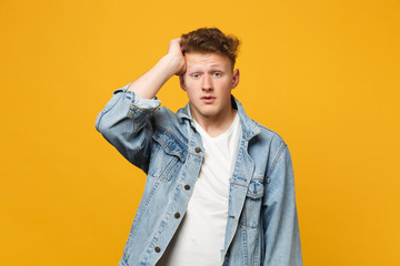Fototapeta premium Portrait of preoccupied young man in denim casual clothes looking camera putting hand on head isolated on yellow orange wall background. People sincere emotions, lifestyle concept. Mock up copy space.