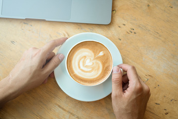 A cup of coffee on desk, Cup of coffee in hand, Men hand hold mug of latte coffee, Close up concept.