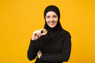 Young arabian muslim woman in hijab black clothes hold in hand holding bitcoin coin currency...