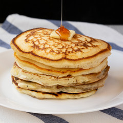 Homemade pancakes with butter and maple syrup on a white plate, side view. Close-up.