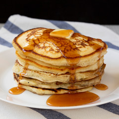 Homemade pancakes with butter and maple syrup on a white plate, side view. Closeup.