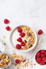 Greek yogurt in bowl with raspberries and muesli on white stone table top view. Healthy breakfast.