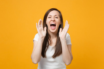 Portrait of cheerful young woman in white casual clothes looking camera, screaming with hand gesture isolated on yellow orange wall background in studio. People lifestyle concept. Mock up copy space.