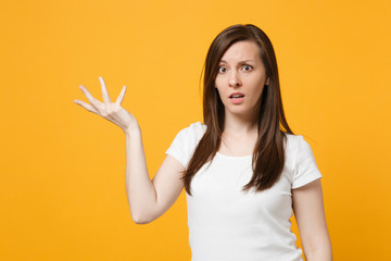 Portrait of perplexed puzzled young woman in white casual clothes looking camera, spreading hand isolated on bright yellow orange background in studio. People lifestyle concept. Mock up copy space.