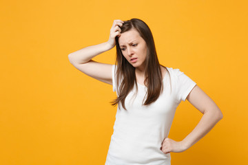 Portrait of preoccupied young woman in white casual clothes looking down, putting hand on head isolated on bright yellow orange wall background in studio. People lifestyle concept. Mock up copy space.