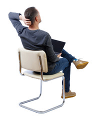 Back view of a man who sits on a chair with a laptop.