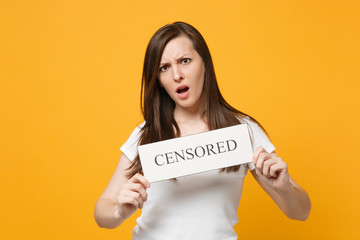 Fototapeta na wymiar Portrait of irritated young woman in white casual clothes holding sign with censored title isolated on bright yellow orange wall background in studio. People lifestyle concept. Mock up copy space.