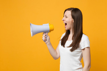 Side view of attractive young woman in white casual clothes looking aside, scream in megaphone isolated on bright yellow orange wall background in studio. People lifestyle concept. Mock up copy space.