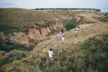 Happy parents and children are walking outdoors in a wheat field and hills view. Back view