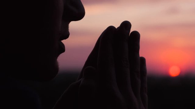 Silhouette of a man meditating or praying at sunset, close up