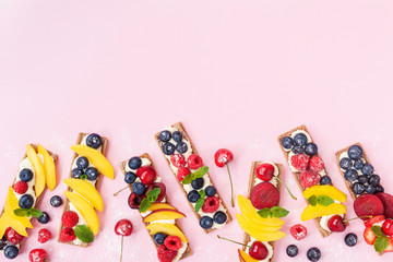 Healthy and organic food snack or dessert from sandwiches with creamy cheese and summer berry fruits on pink trendy background top view. Flat lay.