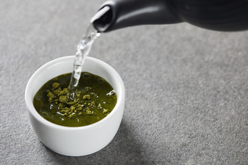 black kettle pouring water in white cup with green matcha powder