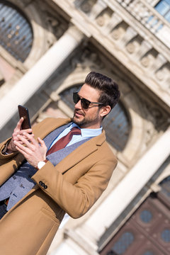 An elegant man on a square using his smartphone