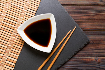 Chopsticks and soy sauce on black stone plate, wooden background with copy space