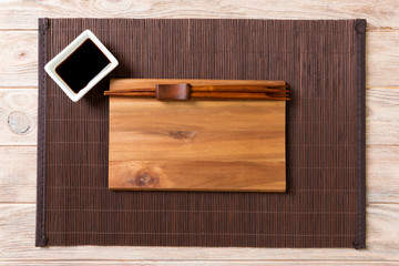 Empty rectangular wooden plate with chopsticks for sushi and soy sauce on wood background. Top view with copy space