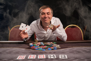 Handsome emotional man is playing poker sitting at the table in casino.