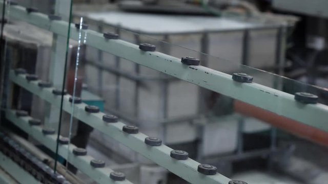 A working man gives glass in belt conveyor for window glass in a manufacturing factory for glass processing and products