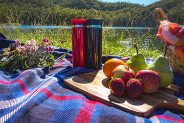 picnic on park lake side in sunny summer season with water bottle and fruits and flowers