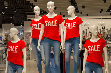 Five mannequins in a row dressed in jeans and red T-shirts with the words "SALE". Front view