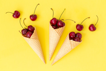 Ice cream cone filled with fresh cherries on a yellow background. Cherry in a waffle cone. Top view. Copy space text. Summer concept. 