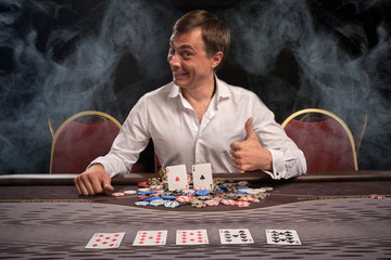 Handsome emotional man is playing poker sitting at the table in casino.