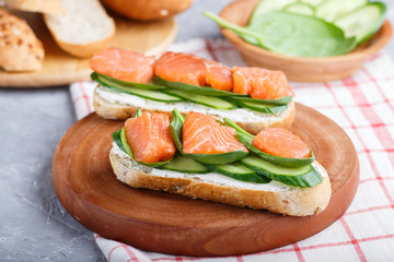 Smoked salmon sandwiches with cucumber and spinach on wooden board on a linen background.