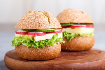 sandwiches with cheese, radish, lettuce and cucumber on wooden board on a gray concrete background.