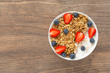 Breakfast smoothie bowl. Healthy smoothie bowl with granola, yogurt, strawberry and fresh blueberries on wooden background. Top view. 