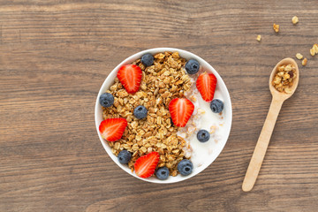 Healthy smoothie bowl with granola, yogurt, strawberry and fresh blueberries on wooden background. Breakfast smoothie bowl, top view.