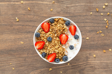 Breakfast smoothie bowl. Healthy smoothie bowl with granola, yogurt, strawberry and fresh blueberries on wooden background. Top view.