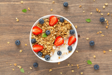 Breakfast smoothie bowl. Healthy smoothie bowl with granola, yogurt, strawberry and fresh blueberries on wooden background. Top view. 