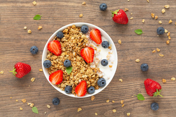 Healthy smoothie bowl with granola, yogurt, strawberry and fresh blueberries on wooden background. Breakfast smoothie bowl, top view.