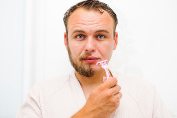 A young man with a shaved face looks into the frame smiling derzhit in the hands of a razor