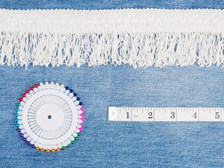 White lace, tape measure, pins on a jeans background. Sewing still life