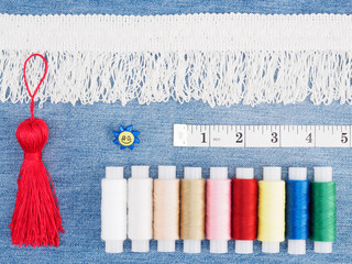 White lace, different color threads, tape measure, button, red brush on a jeans background. Sewing...