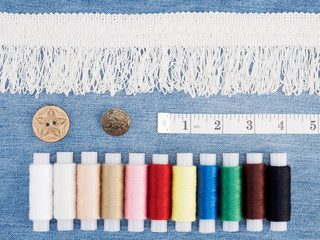 White lace and different color threads, tape measure, buttons on a jeans background. Sewing still...