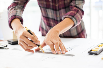 Naklejka premium Construction and building concept. Engineers or architect holding a pen with drawings in construction on blueprints in office.
