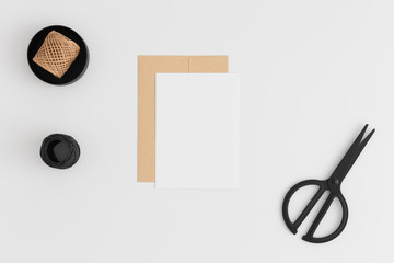 Top view of a white card mockup and envelope with workspace accessories on a white table.